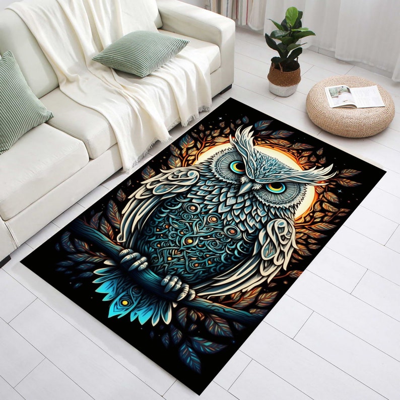 Puede incluir: Una alfombra negra con una ilustraci&oacute;n detallada de un b&uacute;ho azul y blanco posado en una rama. El b&uacute;ho tiene grandes ojos amarillos y patrones intrincados en sus plumas. El fondo presenta una luna dorada y follaje oscuro.