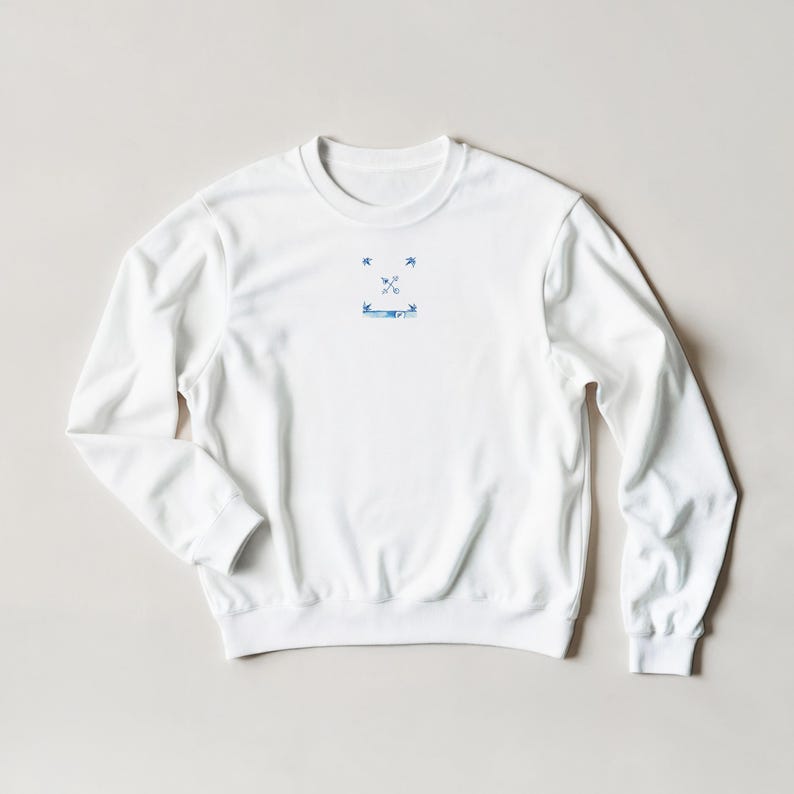 K&ouml;nnte beinhalten: Wei&szlig;es Sweatshirt mit Rundhalsausschnitt und einer kleinen blauen Grafik auf der Brust. Die Grafik zeigt zwei gekreuzte Pfeile, zwei V&ouml;gel und ein Banner. Das Sweatshirt hat lange &Auml;rmel und gerippte B&uuml;ndchen und Saum.
