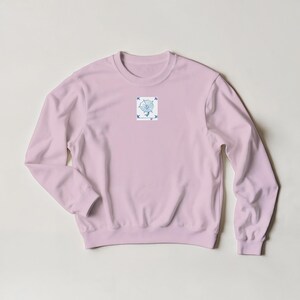 K&ouml;nnte beinhalten: Hellrosa Sweatshirt mit Rundhalsausschnitt und langen &Auml;rmeln. Ein kleines quadratisches Grafikdesign auf der Brust zeigt ein blau-wei&szlig;es Design einer stilisierten Blume und V&ouml;gel.