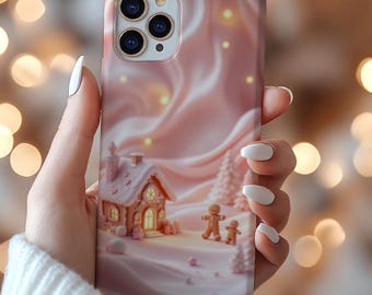 May include: A pink phone case featuring a winter scene with a gingerbread house, two gingerbread people, and a snowy landscape. The case has a glossy finish and is held by a person with white nail polish.