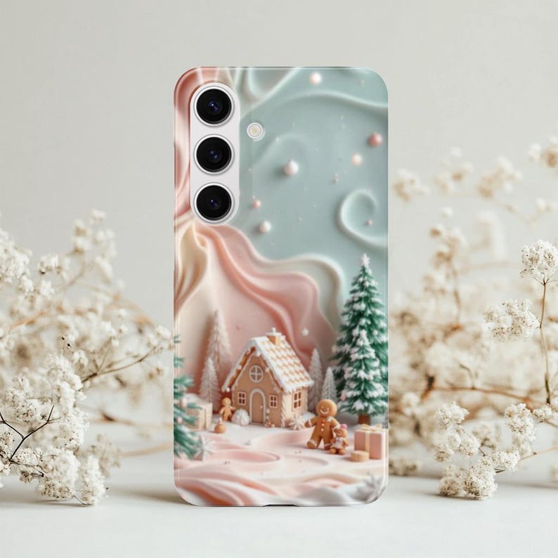 May include: A phone case featuring a winter scene with a gingerbread house, gingerbread people, and Christmas trees. The case has a pastel color palette of pink, blue, and white, with a textured, 3D-like design. The case is designed for a Samsung phone.