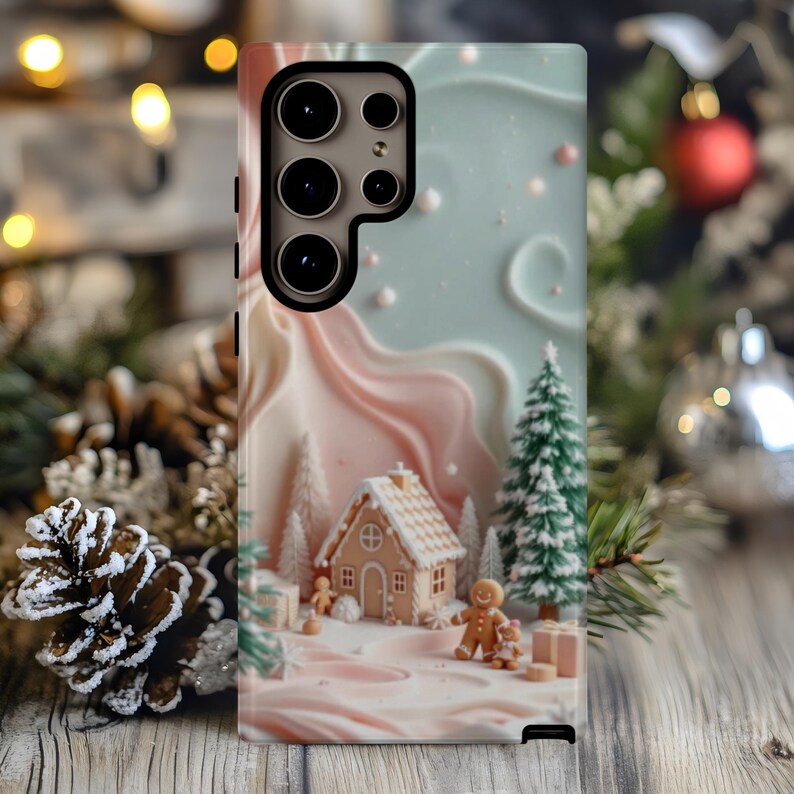 May include: A phone case featuring a whimsical Christmas scene. The design includes a gingerbread house, gingerbread people, snow-covered trees, and a pastel color palette of pink, blue, and white. The case is designed to fit a smartphone.