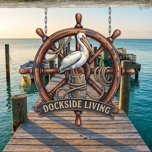 Puede incluir: Un timón de madera con un pelícano posado en un poste de madera, con las palabras "DOCKSIDE LIVING" en una pancarta. La imagen está ambientada en un muelle de madera con un océano tranquilo al fondo.