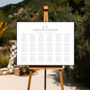 以下が含まれることがあります： 白地に黒と白のシンプルなデザインの結婚式席次表。ゲストの名前と割り当てられたテーブルが記載されています。イーゼルに表示されています。