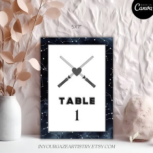 May include: A printable table number card measuring 5x7 inches with a black and white galaxy background. The card features a white heart with two crossed lightsabers and the text "TABLE 1".
