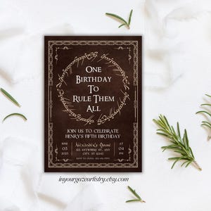 Könnte beinhalten: Eine braune Einladungskarte mit goldener Umrandung und einer goldenen Inschrift, die "One Birthday To Rule Them All" lautet. Die Inschrift befindet sich in einem Kreis mit einem Design, das dem Einen Ring aus dem Herrn der Ringe ähnelt. Die Karte enthält auch den Text "Join us to celebrate Henry's Fifth Birthday" und Details zur Veranstaltung.