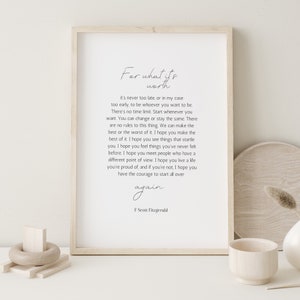 Può includere: Una stampa da parete rettangolare verticale in una cornice di legno chiaro con il testo For what it's worth, it's never too late, or in my case too early, to be whoever you want to be. La citazione è attribuita a F Scott Fitzgerald.