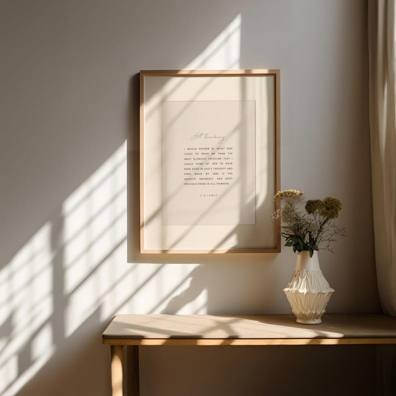 May include: A framed print with the text "All Thinking" and a quote by C.S. Lewis. The print is in a light wood frame, hanging above a wooden table. A white vase with dried flowers sits on the table.