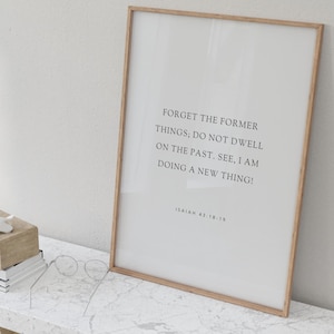 Könnte beinhalten: Ein gerahmter Druck mit einem hellen Holzrahmen. Der Druck hat einen weißen Hintergrund mit schwarzem Text, der lautet: "VERGESST DAS FRÜHERE; VERWEILT NICHT IN DER VERGANGENHEIT. SIEHE, ICH TUE ETWAS NEUES!" und "JESAJA 43:18-19".