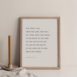 May include: A framed print with a light beige background features the text of Psalm 27:4. The frame is a light wood color. A tan candle sits to the left of the frame in a beige holder.