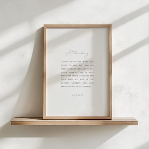 May include: A framed print with the text "All thinking" and a quote by C.S. Lewis. The quote is in black font on a white background, framed by a light brown wooden frame. The print is displayed on a light brown wooden shelf.