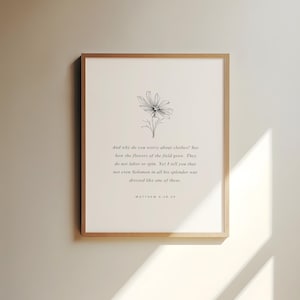 以下が含まれることがあります： 黒と白の花のイラストとマタイによる福音書6:28-29からの引用が特徴の額入りプリント。テキストはシンプルでエレガントなフォントで、フレームは明るい木の色合いです。インテリアに自然とインスピレーションをもたらすアート作品。