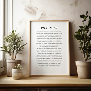 May include: A framed wall art print featuring the text of Psalm 62 in black serif font on a white background. The frame is a light wood tone. The print displays the full biblical passage starting with the title PSALM 62 in bold capital letters.