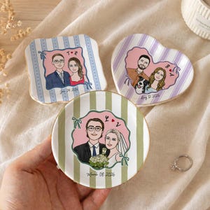 May include: Three ceramic trinket dishes featuring custom illustrations of couples. One square dish with blue stripes, one heart-shaped dish with purple stripes, and one round dish with green stripes. Each dish displays names, dates, and portraits.