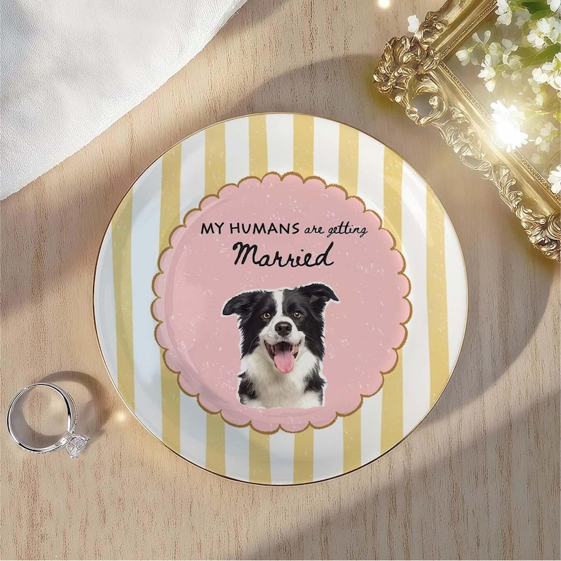 May include: A round ceramic plate featuring vertical yellow and white stripes. The center has a pink scalloped circle with a black and white border collie illustration and the text "MY HUMANS are getting Married" in black lettering.