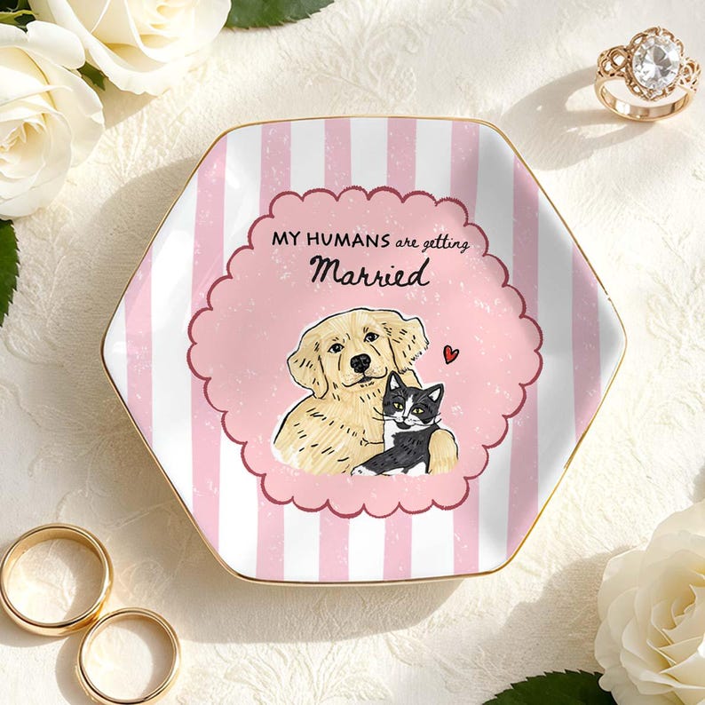 May include: A hexagonal ceramic ring dish featuring a pink and white striped pattern with a scalloped central frame. The text reads MY HUMANS are getting Married above an illustration of a golden retriever and a black and white cat with a small red heart.