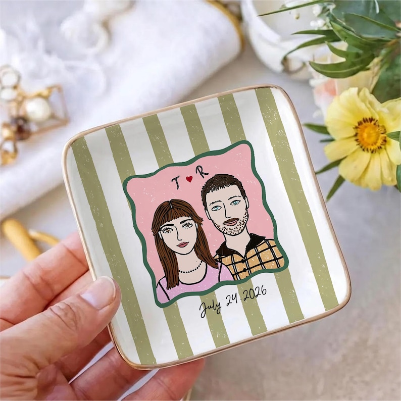 Pu&ograve; includere: Un piattino quadrato in ceramica con bordo dorato, caratterizzato da un motivo a righe verticali bianche e verde salvia. Al centro &egrave; presente un'illustrazione personalizzata di due persone, il testo T R con un cuore e la data July 24, 2026.