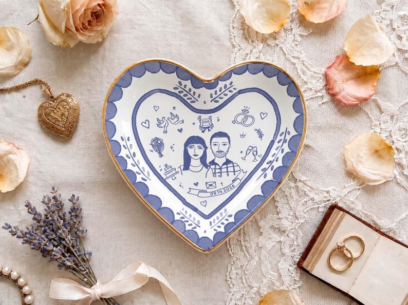 Puede incluir: Un plato de cer&aacute;mica en forma de coraz&oacute;n con borde dorado y cenefa festoneada azul. El centro presenta una ilustraci&oacute;n lineal de una pareja, iconos de boda y una cinta con la fecha 09.14.2026 impresa en tinta azul oscuro.