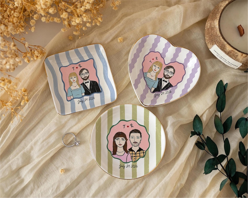 Pu&ograve; includere: Tre piattini in ceramica con illustrazioni personalizzate di coppie. Un piattino quadrato a righe blu, uno a forma di cuore a righe viola e uno rotondo a righe verdi. Ogni piattino mostra un ritratto, le iniziali T R e July 24 2026.