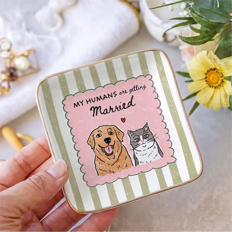 May include: A square ceramic trinket dish with a gold-toned rim, featuring a light green and white vertical striped background. The center displays a pink scalloped frame with a golden retriever and a gray cat, plus the text MY HUMANS are getting Married.