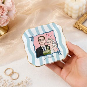 May include: A square ceramic trinket dish with wavy edges and a gold-painted rim. The dish features a light blue and white striped pattern and a central illustration of a couple with the text T heart R and the date Jan 24, 2026.