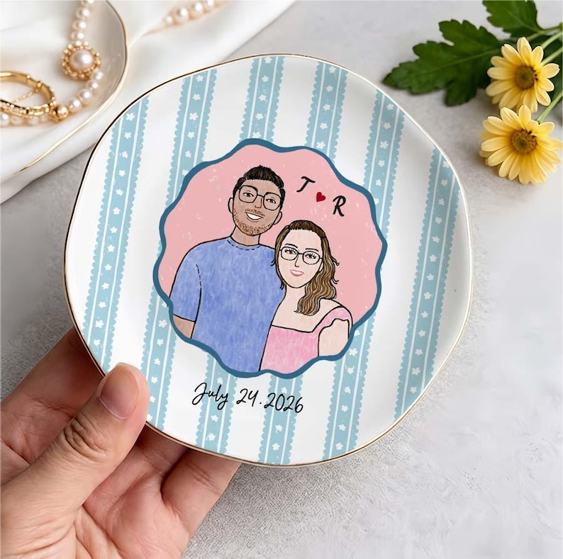 Pu&ograve; includere: Un piattino rotondo in ceramica con un motivo a righe verticali azzurre e bianche e una cornice centrale rosa smerlata. L'illustrazione raffigura una coppia con occhiali, le iniziali T e R con un cuore rosso e la scritta July 24, 2026.