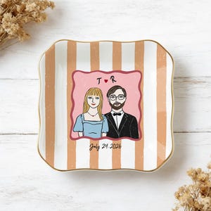 Pu&ograve; includere: Un piattino quadrato in ceramica con bordi ondulati e un bordo dorato. La superficie presenta strisce verticali color pesca e bianche. Un'illustrazione centrale raffigura una coppia con il testo T R, un cuore rosso e la data July 24, 2026.