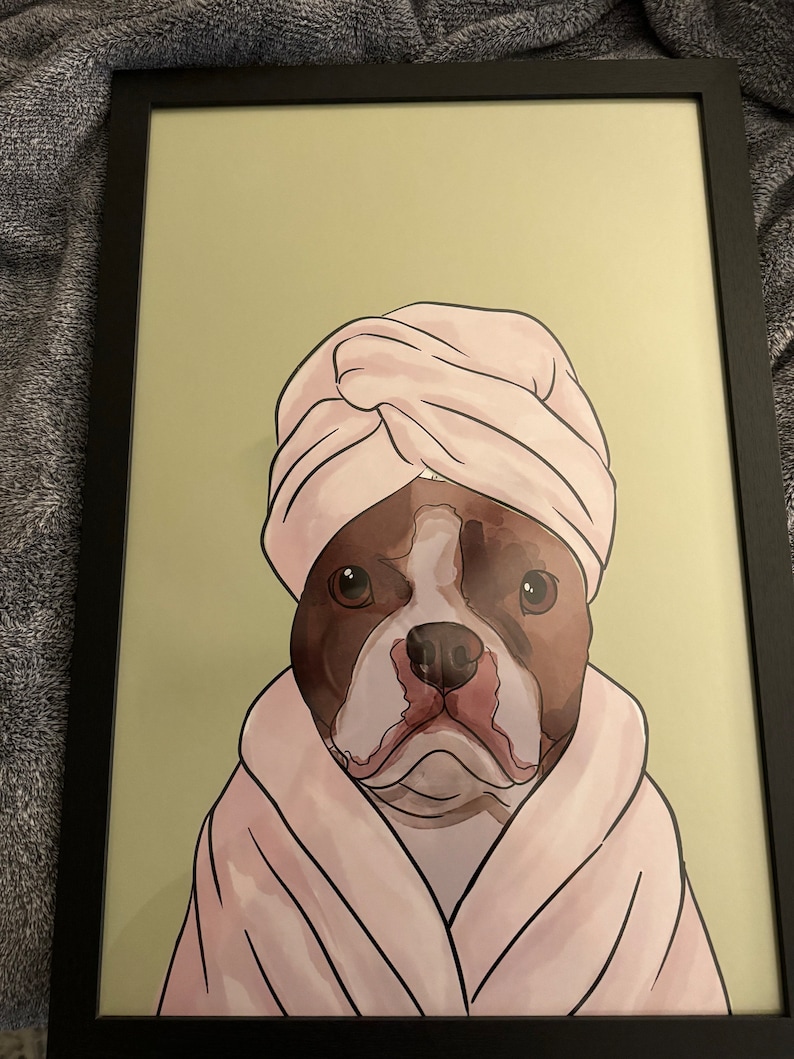 May include: A brown and white dog wearing a pink bathrobe and a pink towel on its head. The dog is looking directly at the viewer.
