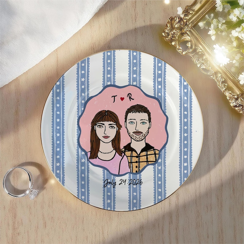 Pu&ograve; includere: Un piatto rotondo in ceramica con un motivo a righe verticali blu e bianche e piccole stelle. Al centro, un emblema rosa smerlato mostra un'illustrazione di due persone, il testo T cuore R e la data 24 luglio 2026.