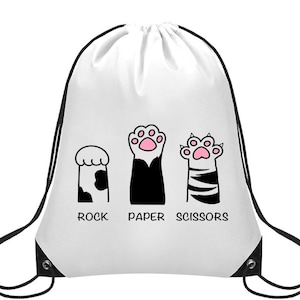 May include: White drawstring bag with a fun design of cat paws representing "Rock, Paper, Scissors." The paws are black and white with pink paw pads. The words "ROCK", "PAPER", and "SCISSORS" are printed below the paws.