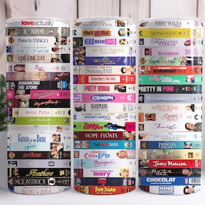May include: Three cylindrical tumblers are decorated with images of VHS tapes. Each tumbler is covered in movie titles like "Love Actually," "Clueless," and "Pretty Woman." The tumblers are arranged in a row against a white background.