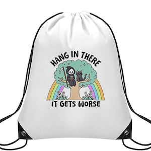 May include: White drawstring bag featuring a cartoon illustration of a grim reaper and a black cat sitting in a tree above a rainbow. The text "HANG IN THERE IT GETS WORSE" is printed above and below the image in black.