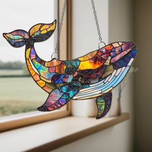 May include: A stained glass whale hanging from a silver chain. The whale is made of iridescent glass pieces in shades of blue, purple, yellow, and orange.