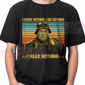 May include: A black t-shirt with a vintage-style image of a man in a military uniform. The text "I know nothing I see nothing I hear nothing" is printed on the shirt.