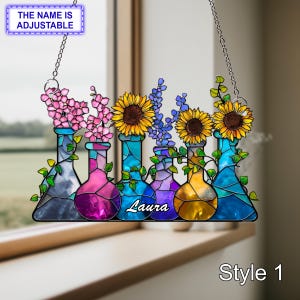 Könnte beinhalten: Buntglas-Fensteraufhänger mit fünf bunten Bechern, die mit Blumen gefüllt sind. Die Becher sind in Blau-, Lila- und Gelbtönen gehalten, mit rosa und gelben Blumen. Der Name "Laura" steht auf einem Becher. Der Text "Style 1" steht unten.