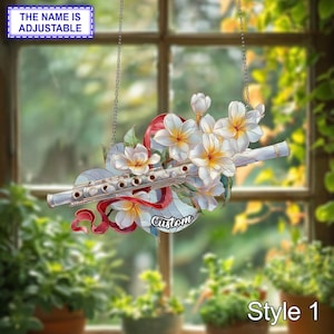Puede incluir: Adorno colgante decorativo con una flauta plateada, flores blancas con centros amarillos y una cinta roja. Los textos "The Name is Adjustable" y "Custom" son visibles. El diseño está etiquetado como "Style 1".