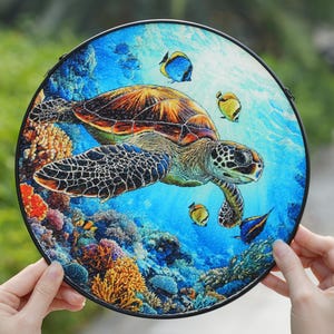 May include: Round decorative art piece featuring a sea turtle swimming among colorful coral and fish. The artwork has a black border and is set against a blue ocean background. The turtle has a brown shell and patterned flippers.