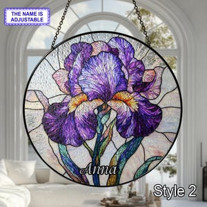 May include: Round stained glass window featuring a purple iris flower with yellow accents and green stems. The name "Anna" is displayed on the flower. The text "Style 2" is also visible. The window is suspended by a chain.