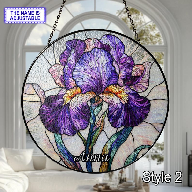 May include: Round stained glass window featuring a purple iris flower with yellow accents and green stems. The name "Anna" is displayed on the flower. The text "Style 2" is also visible. The window is suspended by a chain.