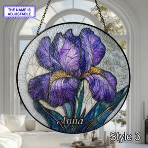 May include: A round stained glass panel featuring a purple iris flower with yellow accents and green leaves. The panel is framed in black and hangs from a chain. The name "Anna" is written on the panel, with the text "Style 3" at the bottom.