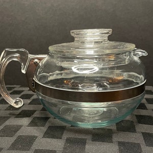 May include: A clear glass teapot with a silver band around the middle. The teapot has a handle and a lid.
