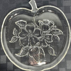 May include: A clear glass apple-shaped serving dish with a floral design. The dish features a large flower with a smaller flower and leaves.