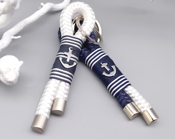 May include: Two nautical-themed keychains. One is white, the other is navy blue. Each keychain features a silver anchor charm and is wrapped with navy blue and white striped rope. The ends are finished with silver-colored metal.