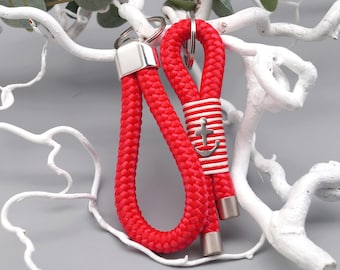 May include: Two red rope keychains with silver-toned metal accents. One keychain features a white and red striped band with a silver anchor charm. The keychains are displayed against a white branch background.