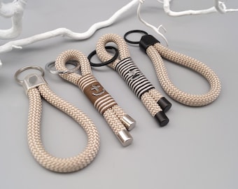 May include: Four beige rope keychains with metal rings and different accents. One keychain has a black and white striped pattern, another has a brown anchor design, and two have a simple beige rope design.