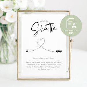 May include: A framed sign with the word "Shuttle" in elegant script, with a dotted line forming a heart and leading to a bus icon. The sign includes text in German and a PDF icon, ideal for wedding transportation.