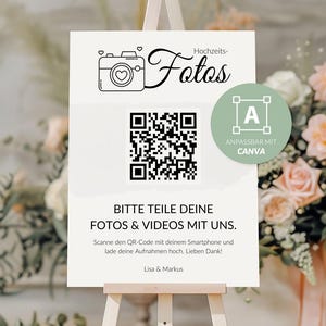 May include: A white sign with a black and white QR code, a camera icon, and the text "Hochzeits-Fotos" (Wedding Photos) in black cursive. The sign also includes the text "Bitte teile deine Fotos & Videos mit uns." (Please share your photos & videos with us.) and "Scanne den QR-Code mit deinem Smartphone und lade deine Aufnahmen hoch. Lieben Dank!" (Scan the QR code with your smartphone and upload your photos. Thanks!) in black. The sign also includes the text "Lisa & Markus" in black. The sign is on a wooden easel and is in front of a bouquet of pink flowers.