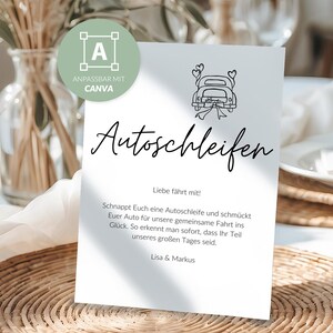 Puede incluir: Una tarjeta blanca con la palabra "Autoschleifen" en escritura elegante, con una ilustración de coche con corazones. La tarjeta incluye texto en alemán, colocada sobre una mesa con un mantel individual tejido y un arreglo floral.