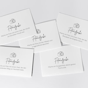 May include: White cards with black text and a camera illustration. The cards have different prompts for taking photos at a wedding, such as taking a photo with a guest from the same school.