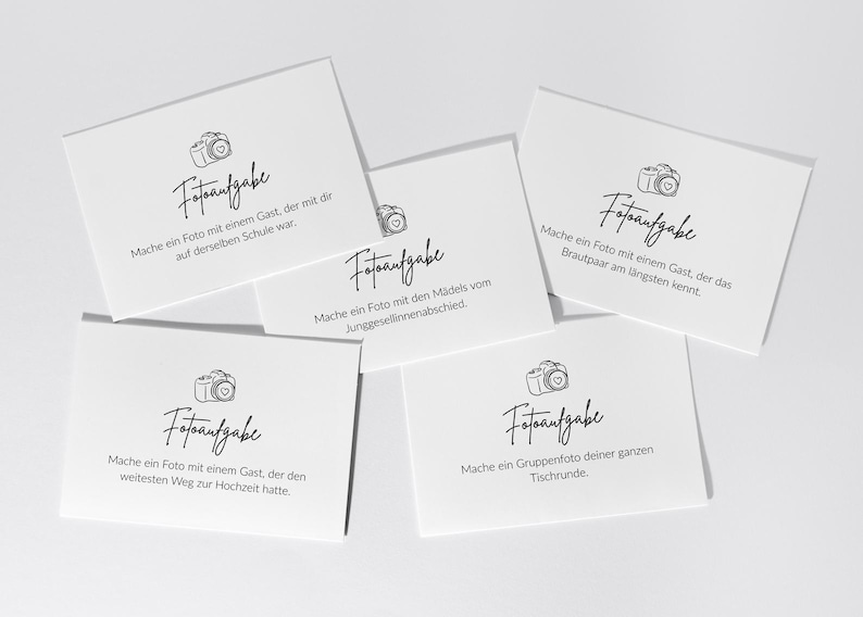 May include: White cards with black text and a camera illustration. The cards have different prompts for taking photos at a wedding, such as taking a photo with a guest from the same school.